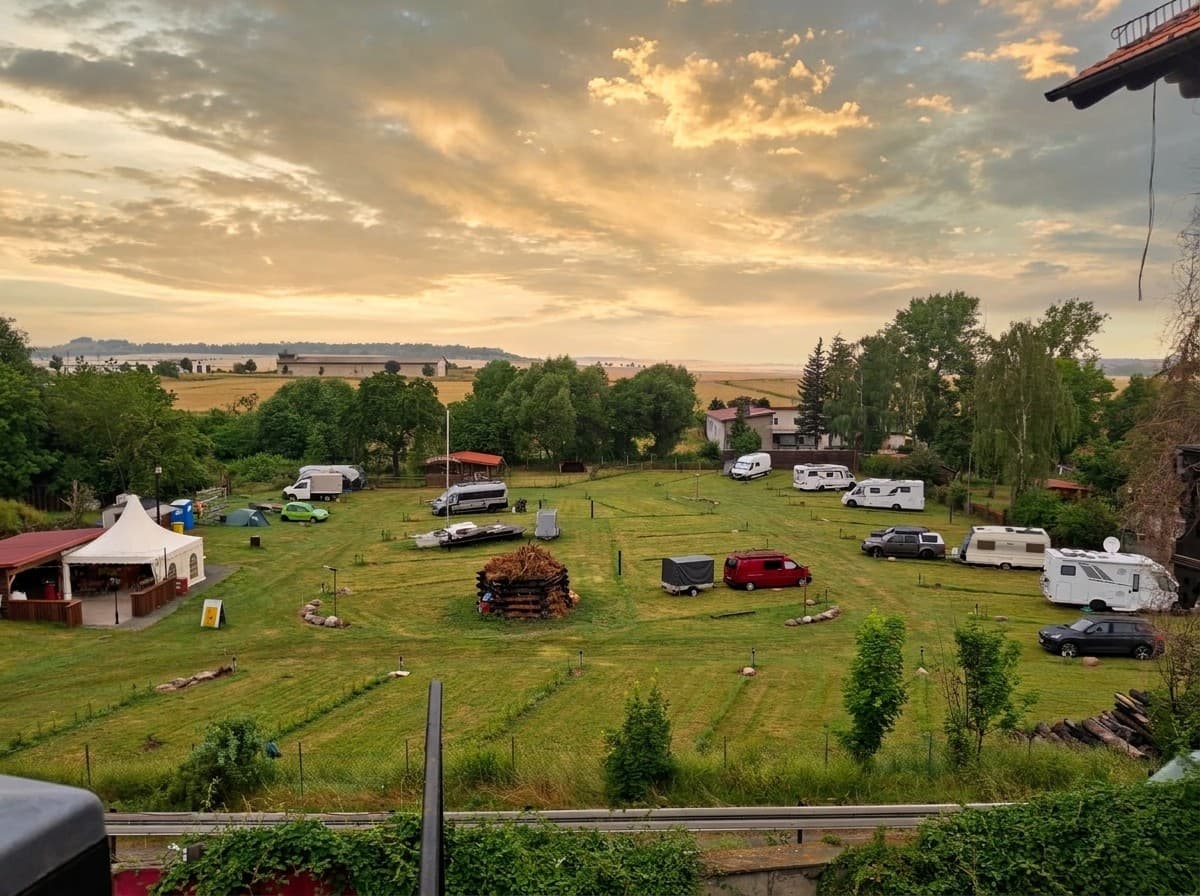Überblick über den Campingplatz Auf der Hohe unter Abendwolken: Wohnmobile und Wohnwagen auf der Wiese, links der Pavillon
